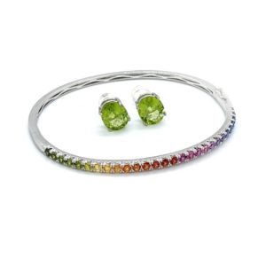 A white gold bangle style bracelet with half covered in a rainbow of sapphires ranging from green through to blue, and large oval peridot studs that matches a green portion of the sapphire rainbow.