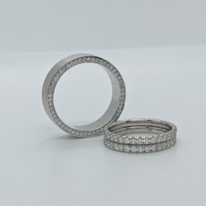 Groom's brushed white gold wedding band with hidden diamonds around the entire side, beside the bride's two white gold pave wedding bands.