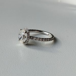 Oval diamond engagement ring with unique double-sided halo and pave band set in white gold.