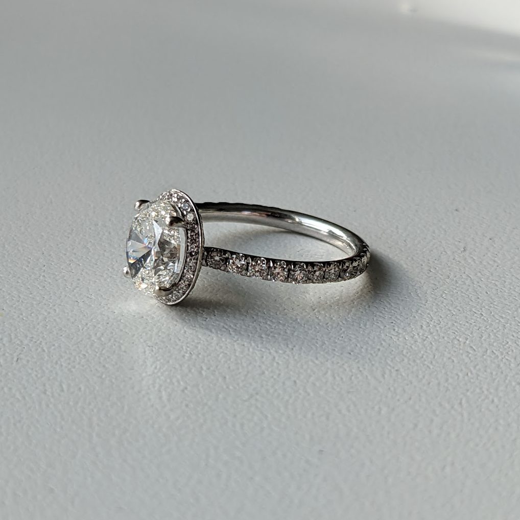 Oval diamond engagement ring with unique double-sided halo and pave band set in white gold.