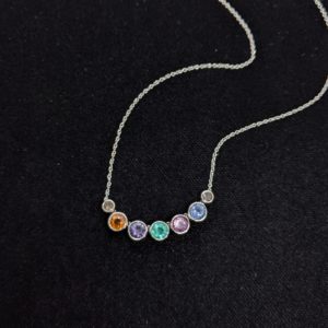 Round precious & semi-precious stones bezel set in white gold that slide along a white gold chain. Each stone represents a different family member and is a different colour -- orange, purple, green, pink, and blue -- bookmarked by two smaller salt & pepper diamonds to represent their dogs.