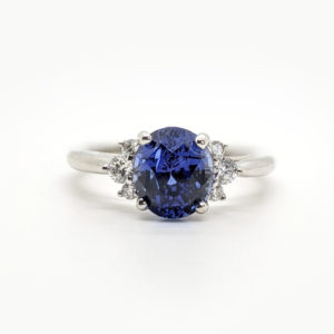 Round blue sapphire with diamond clusters on both sides and a white 14k band.