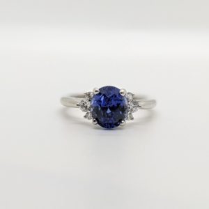 Round blue sapphire with diamond clusters on both sides and a white 14k band.
