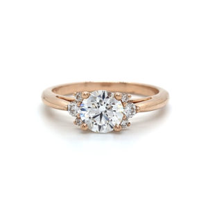 Round diamond engagement ring set with graduated clusters of 3 smaller diamonds on either side, set in rose gold.