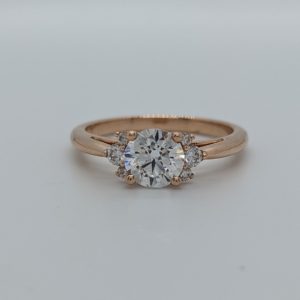 Round diamond engagement ring set with graduated clusters of 3 smaller diamonds on either side, set in rose gold.