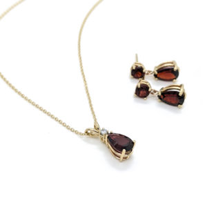 Pear garnet and gold necklace and earring set. Pendant composed of a pear garnet topped with one diamond, and round garnet studs with pear garnets matching the pendant hanging.