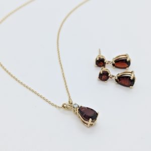 Pear garnet and gold necklace and earring set. Pendant composed of a pear garnet topped with one diamond, and round garnet studs with pear garnets matching the pendant hanging.