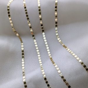 Two yellow gold valentino chain necklaces against cream silk.