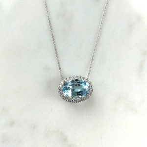 Large oval aquamarine stone with a halo of diamonds, set horizontally on a white gold chain.