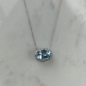 Large oval aquamarine stone with a halo of diamonds, set horizontally on a white gold chain.